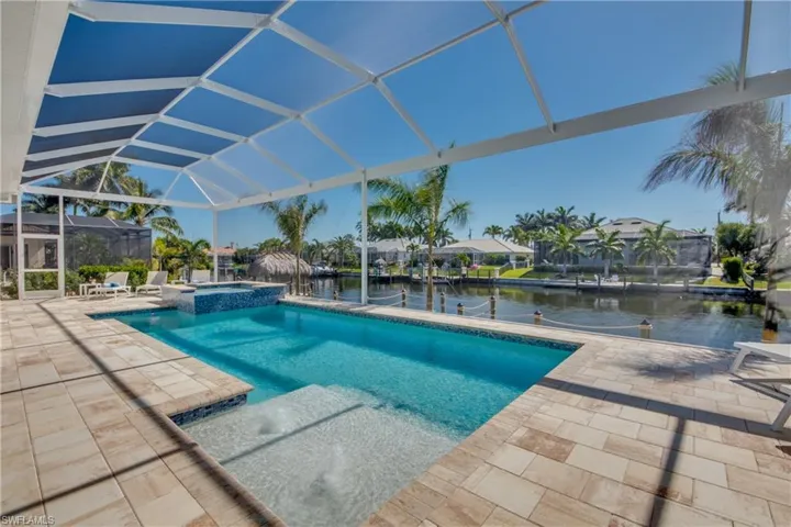 View of swimming pool featuring a patio area, glass enclosure, a sunroom, a water view, and a pool with connected hot tub