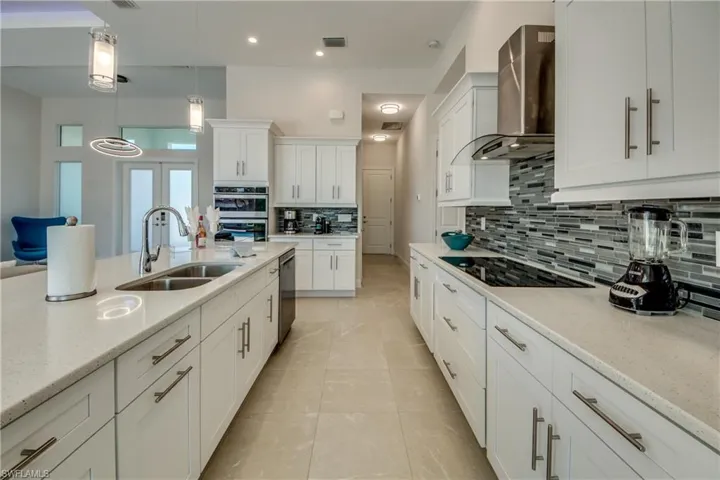 Kitchen with wall chimney range hood, white cabinetry, light stone countertops, hanging light fixtures, and recessed lighting