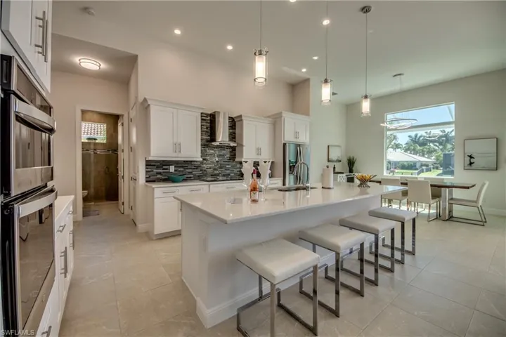 Kitchen with appliances with stainless steel finishes, a kitchen breakfast bar, white cabinetry, wall chimney range hood, and decorative light fixtures