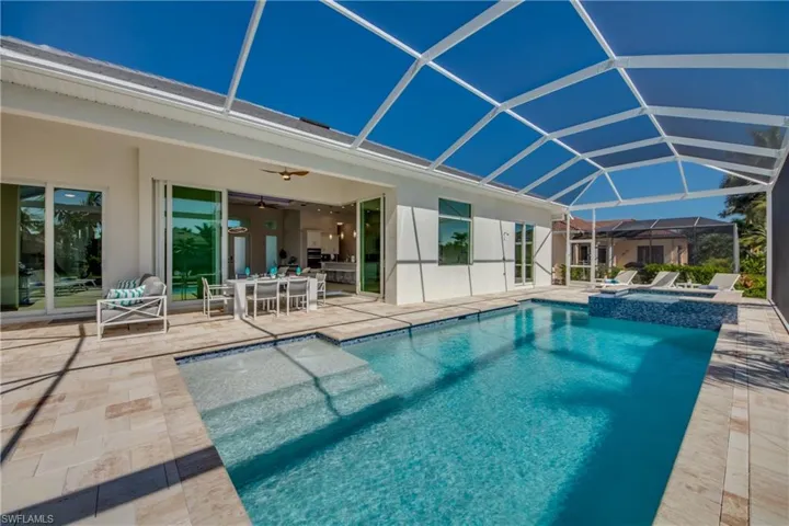 View of pool featuring a sunroom, glass enclosure, a patio, a pool with connected hot tub, and outdoor dining space