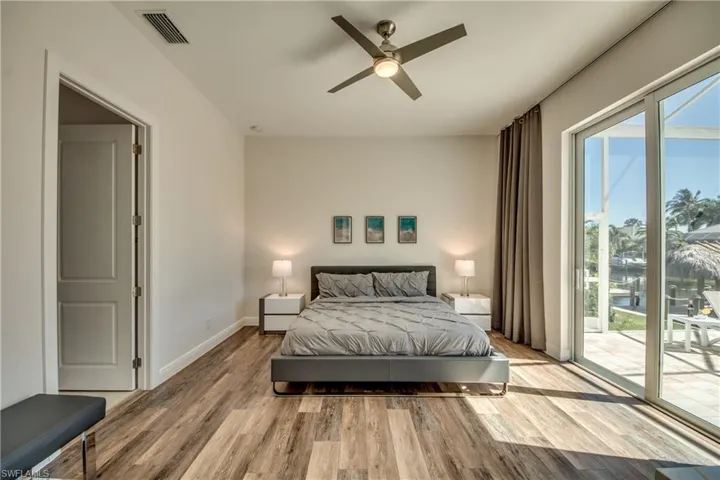 Bedroom with access to outside, light wood-style flooring, a ceiling fan, and a water view