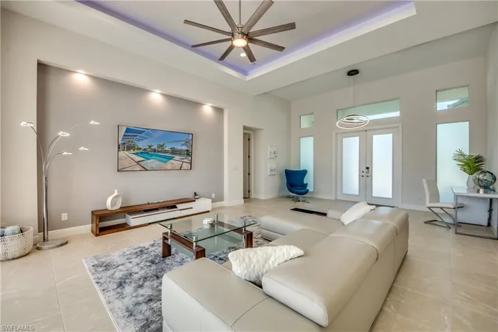 Living area featuring a tray ceiling, french doors, a towering ceiling, ceiling fan, and light tile patterned floors
