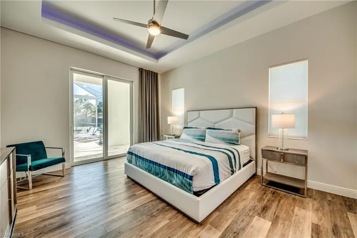 Bedroom with access to exterior, light wood finished floors, a tray ceiling, and a ceiling fan