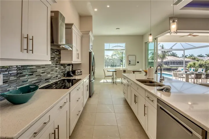 Kitchen featuring light stone counters, wall chimney range hood, decorative backsplash, appliances with stainless steel finishes, and white cabinets