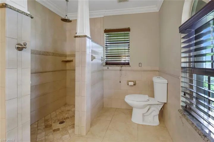Bathroom featuring crown molding, tiled shower, toilet, and tile walls