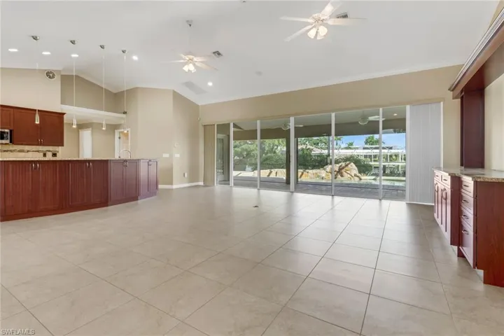 Unfurnished living room with light tile patterned flooring, high vaulted ceiling, ceiling fan, and crown molding