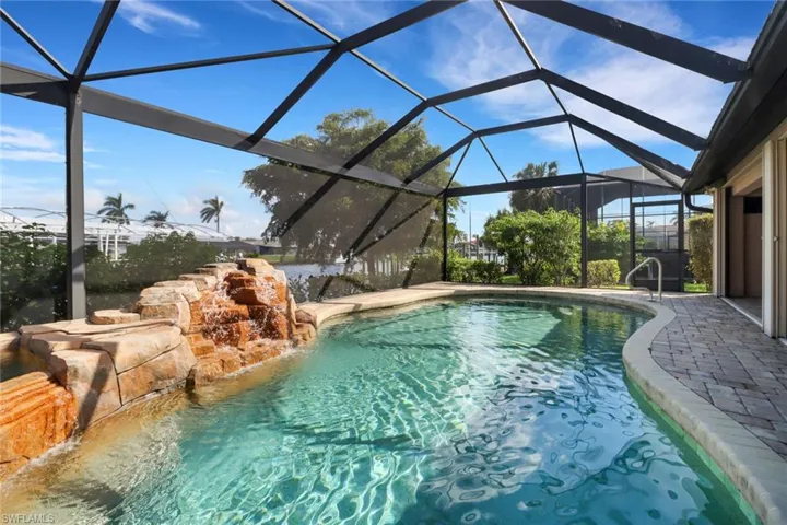 View of pool with glass enclosure, pool water feature, and a patio area