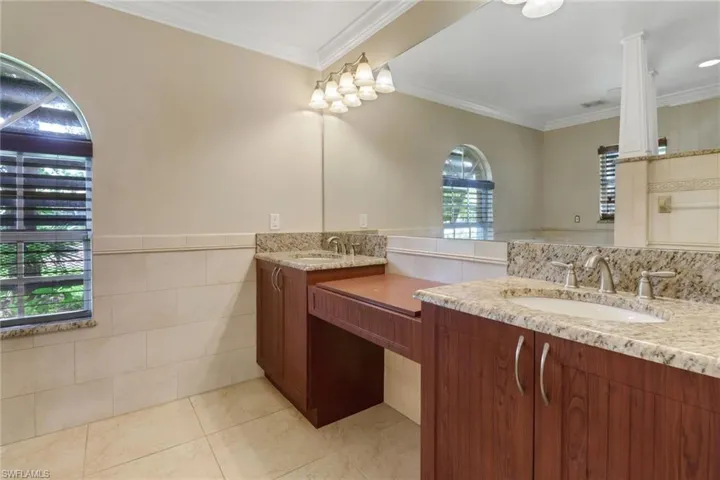 Bathroom with tile patterned flooring, crown molding, vanity, and tile walls
