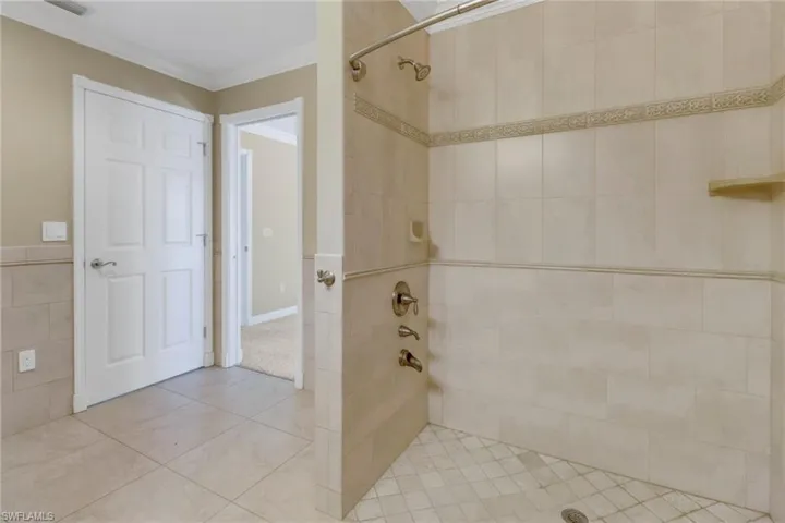 Bathroom with tile patterned flooring, ornamental molding, tiled shower, and tile walls