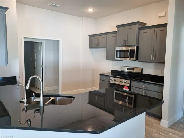 Kitchen with sink, dark stone counters, light hardwood / wood-style floors, gray cabinets, and appliances with stainless steel finishes