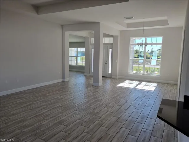 Unfurnished living room with a tray ceiling, plenty of natural light, dark wood-type flooring, and an inviting chandelier