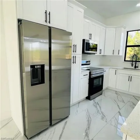 Contemporary kitchen featuring a stainless steel side-by-side refrigerator, white shaker-style cabinetry with matte black hardware, white countertops, and large format tile flooring with a veined pattern
