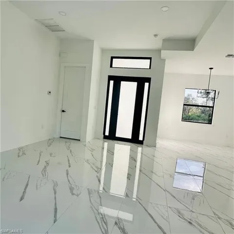 Entry foyer featuring large format porcelain tile flooring, a contemporary black and white front door with sidelights, a transom window, and a modern chandelier