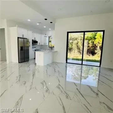 Spacious living area featuring large format, high-gloss tile flooring with grey veining, a contemporary kitchen with white cabinetry and stainless steel appliances, a kitchen island with seating, and large sliding glass doors providing access to the exterior