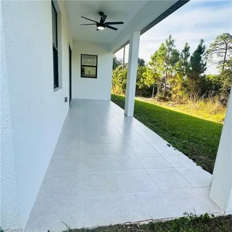 Expansive covered patio featuring light-toned tile flooring, a modern black ceiling fan with integrated lighting, and a stucco exterior