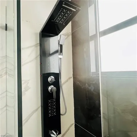 Modern shower system featuring a black panel with integrated rainfall showerhead, handheld sprayer, and body jets