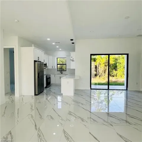 Open-concept living area featuring large format white and gray veined tile flooring, a modern kitchen with white cabinetry and stainless steel appliances, and sliding glass doors leading to outdoor space