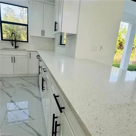 Kitchen featuring speckled light-toned countertops, white cabinetry with matte black hardware, and an undermount sink with a matte black faucet