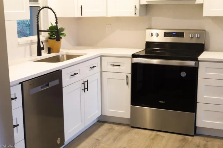 Kitchen with exhaust hood, stainless steel appliances, sink, light wood-type flooring, and white cabinets