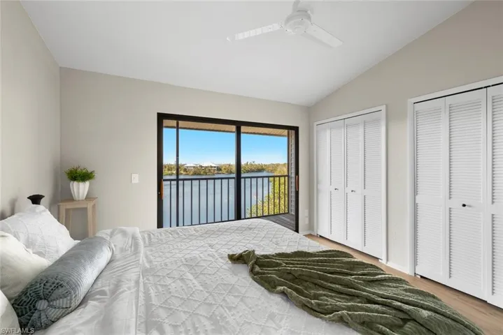 Bedroom with lofted ceiling, a water view, multiple closets, access to exterior, and wood finished floors