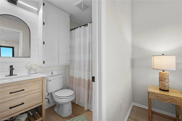 Bathroom featuring a shower with curtain, vanity, toilet, visible vents, and wood finished floors