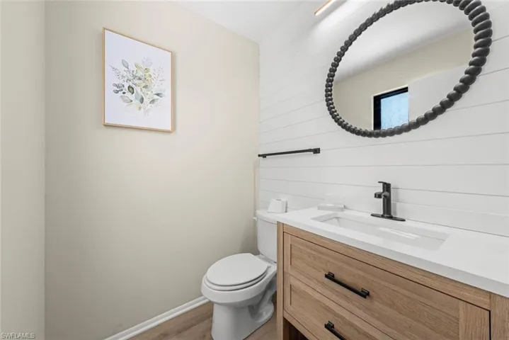 Half bathroom with baseboards, wood finished floors, toilet, and vanity