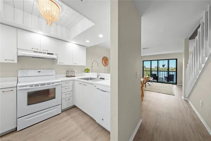 Kitchen with light countertops, a sink, under cabinet range hood, white appliances, and white cabinets