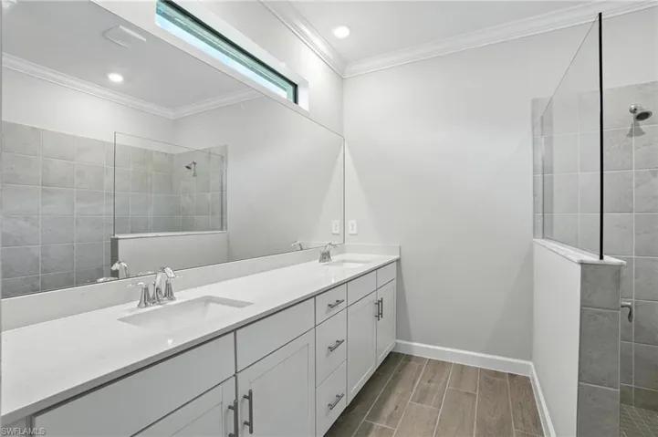 Bathroom with a walk in shower, double vanity, wood finish floors, and crown molding