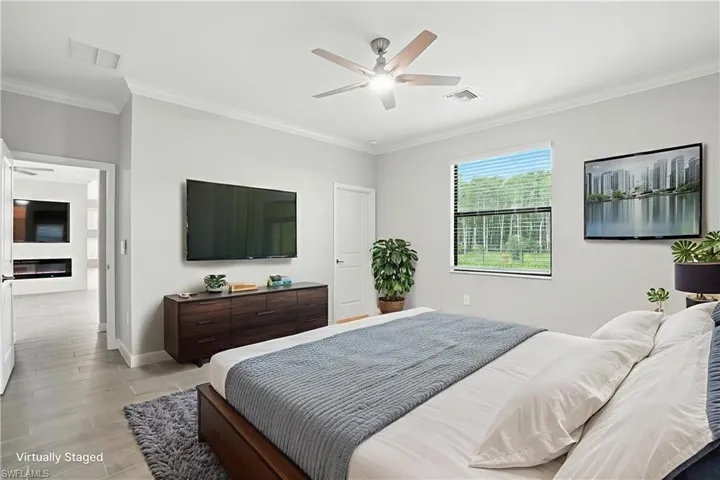 Bedroom featuring ornamental molding, light wood-style flooring, a ceiling fan, and a glass covered fireplace
