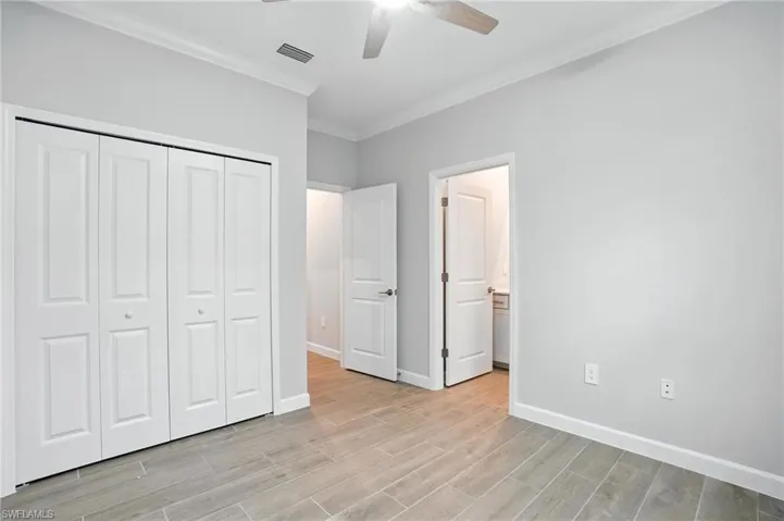 Unfurnished bedroom with crown molding, light wood-style floors, a closet, ceiling fan, and ensuite bath