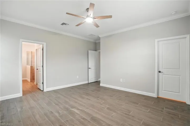 Unfurnished bedroom featuring crown molding, wood finished floors, ensuite bathroom, and ceiling fan