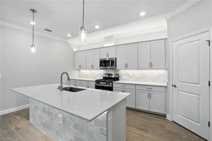 Kitchen with stainless steel appliances, ornamental molding, wood finished floors, decorative backsplash, and a kitchen island with sink