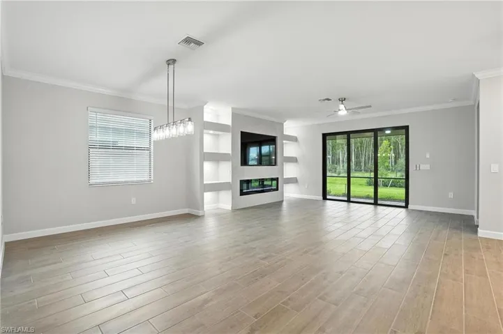 Unfurnished living room featuring ceiling fan, a fireplace, light wood-type flooring, crown molding, and built in features