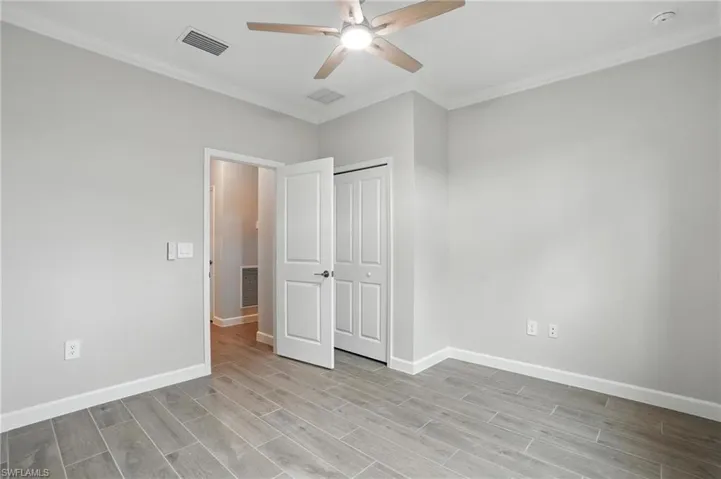 Unfurnished bedroom featuring crown molding, wood finished floors, a closet, and a ceiling fan