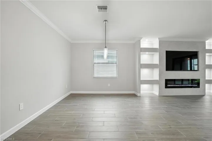 Unfurnished living room featuring crown molding, built in shelves, a large fireplace, and wood finished floors