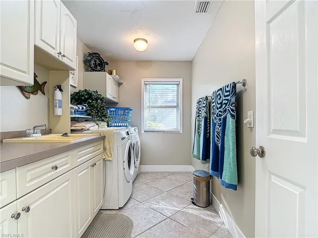 Laundry area featuring sink, cabinets, washing machine and dryer, a textured ceiling, and light tile patterned flooring
