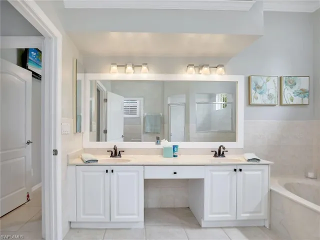 Primary Bathroom with Dual Sinks, Framed Vanity Mirror, Soaking Tub, Walk-In Shower with Glass Enclosure, and Crown Molding