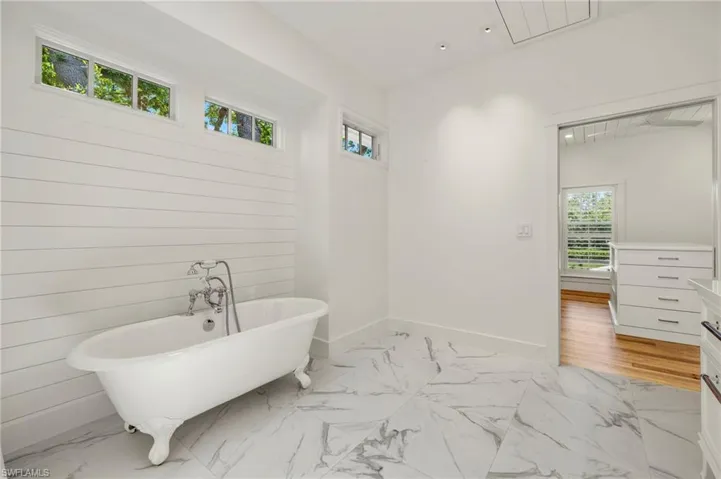 Primary bathroom with light marble finish flooring, a soaking tub, vanity, and recessed lighting