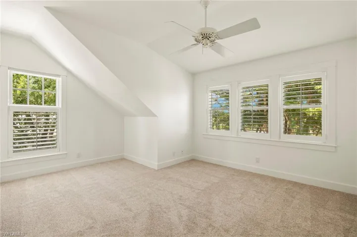 Upstairs first bedroom featuring light colored carpet, vaulted ceiling, plenty of natural light, and a ceiling fan