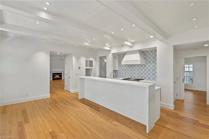 Kitchen with recessed lighting, backsplash, beam ceiling, a warm lit fireplace, and custom range hood