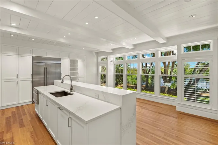 Kitchen featuring white cabinets, light stone countertops, light wood-style floors, stainless steel built in fridge, and a kitchen island with sink