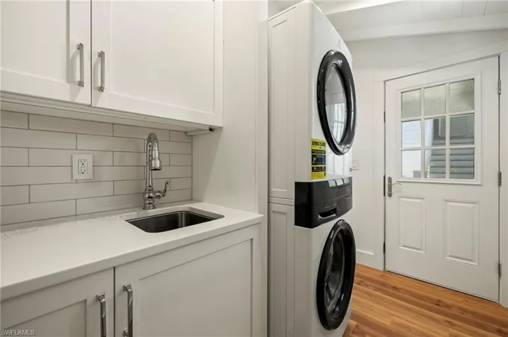 Laundry area featuring stacked washer / dryer, cabinet space, light wood-style floors, and lofted ceiling