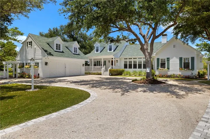 New England style home with gravel driveway, a porch, a garage, and a front lawn