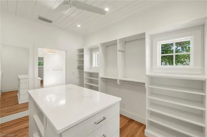 Primary walk-in spacious closet with light wood-type flooring and a chandelier