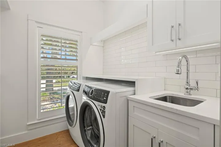 Primary laundry area with light wood-style flooring, cabinet space, and washer and dryer