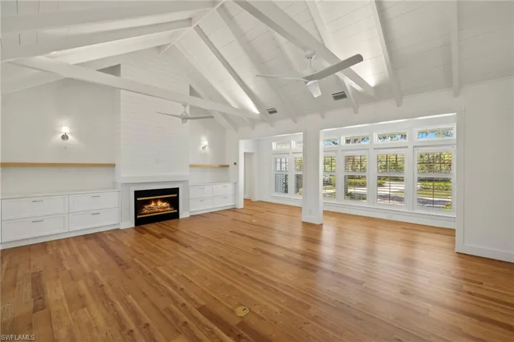Unfurnished living room with a fireplace, light wood-style floors, beam ceiling, high vaulted ceiling, and a ceiling fan