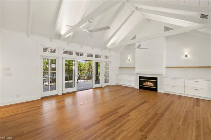 Unfurnished living room featuring a large fireplace, high vaulted ceiling, light wood-style flooring, beamed ceiling, and ceiling fan