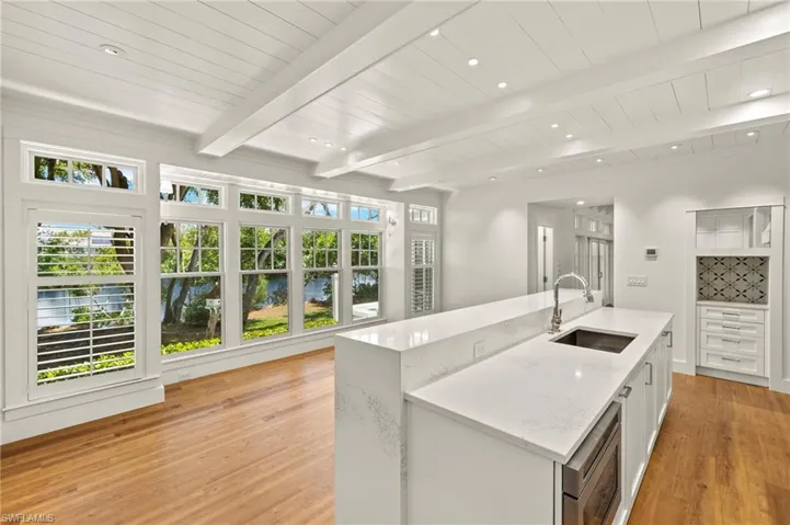 Kitchen with light stone counters, a kitchen island with sink, light wood-style floors, white cabinetry, and stainless steel microwave