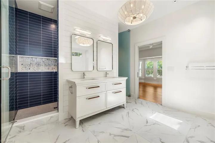 Primary bathroom featuring double vanity, light marble finish flooring, and a stall shower
