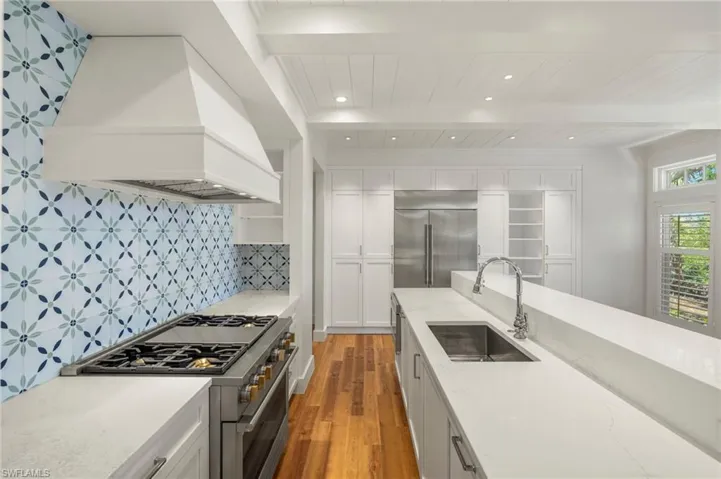 Kitchen featuring high end appliances, custom exhaust hood, dark wood-style floors, light stone counters, and recessed lighting